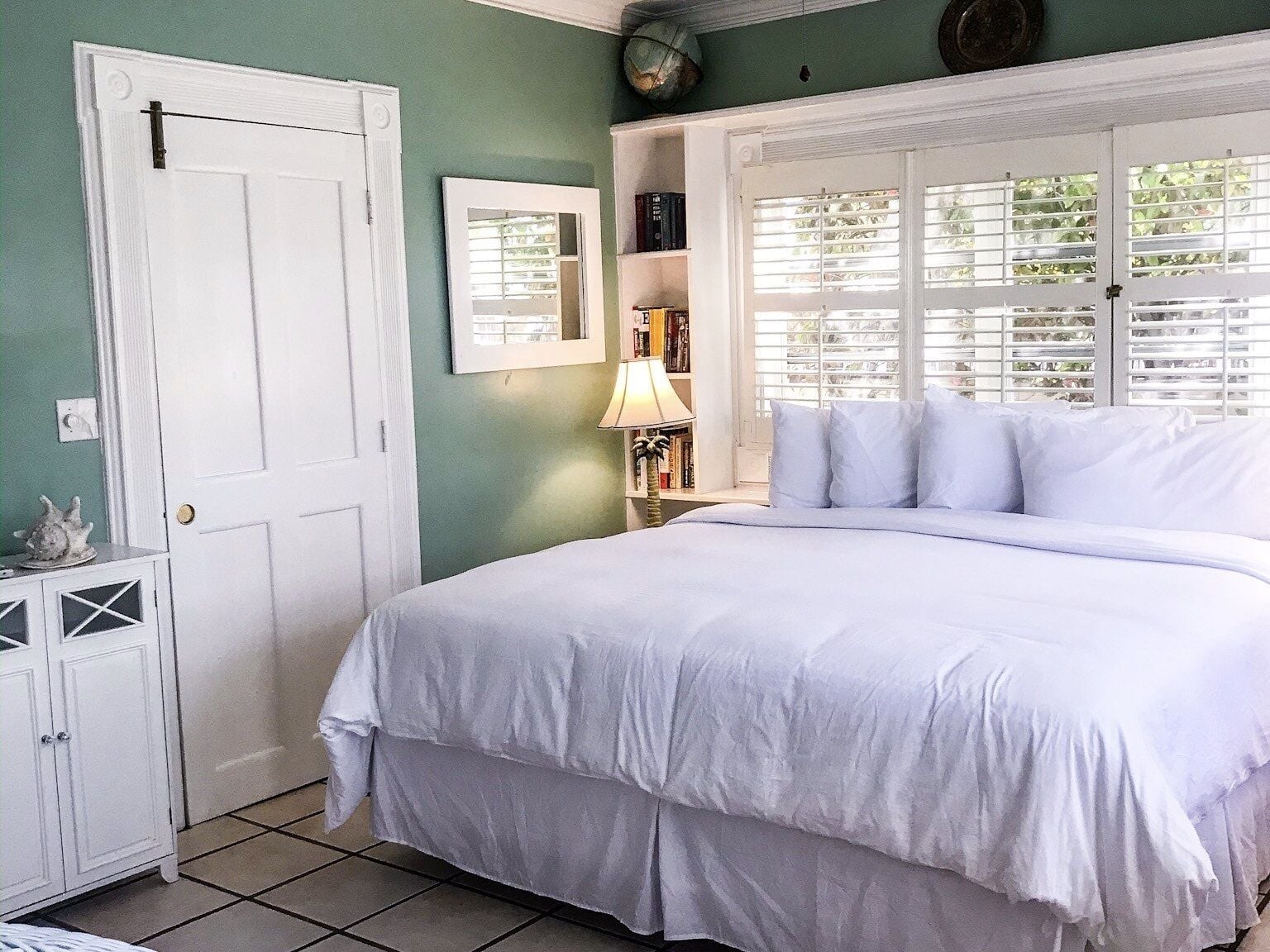 A bedroom with a bed, a nightstand, a lamp, a bookshelf, and a door.