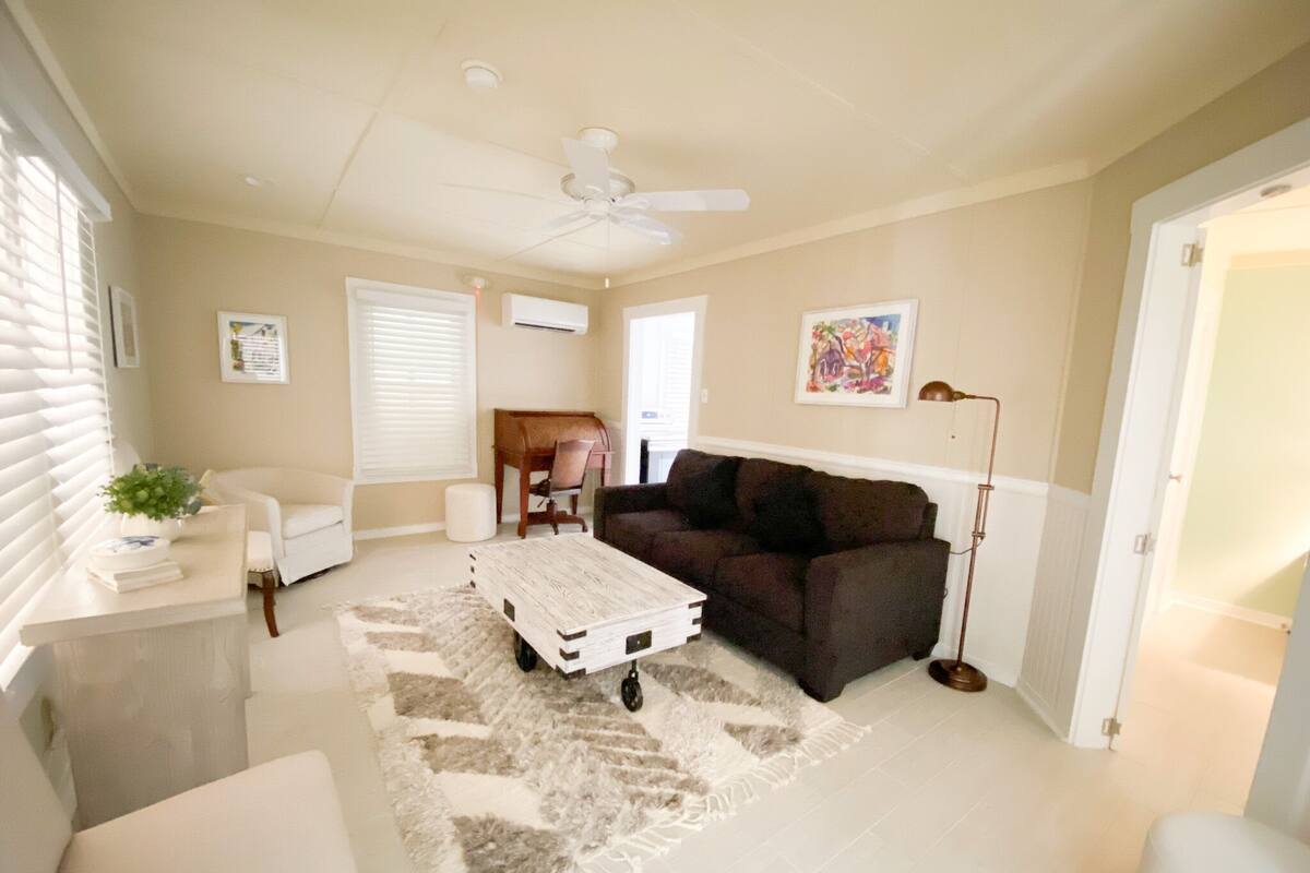 A living room with a dark brown sofa, a white armchair, a coffee table, and a ceiling fan.