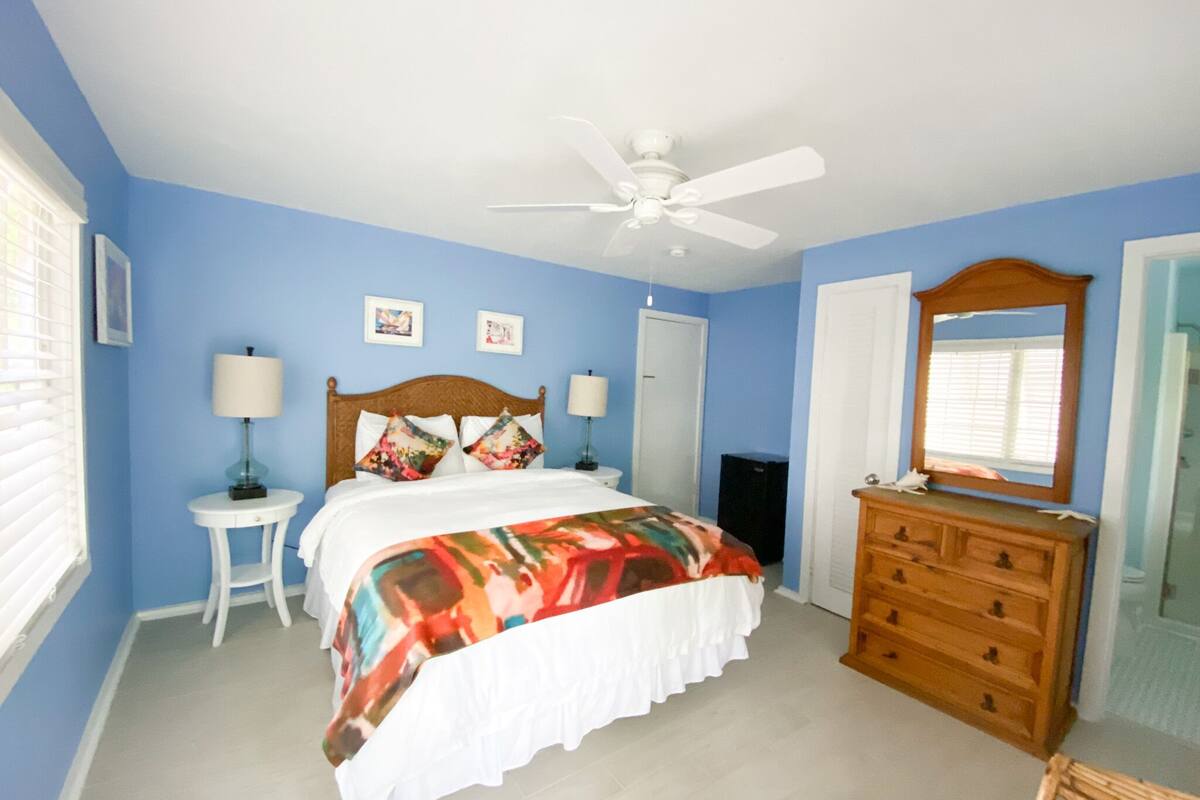 A bedroom with a bed, a dresser, a ceiling fan, and a mirror.