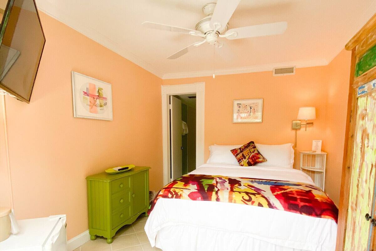A bedroom with a bed, a ceiling fan, a green dresser, a white radiator, and a door leading to another room.