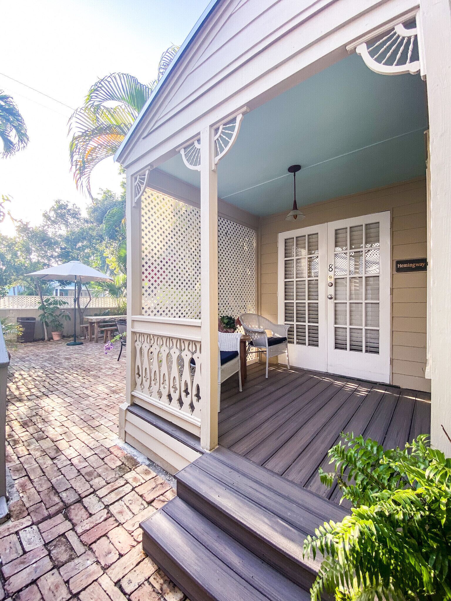 A covered porch with a wooden deck, a white door with glass panels, and a sign reading "Hemingway Way".