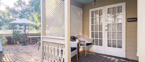 A covered porch with a wooden deck, a white door with glass panels, and a sign reading "Hemingway Way".