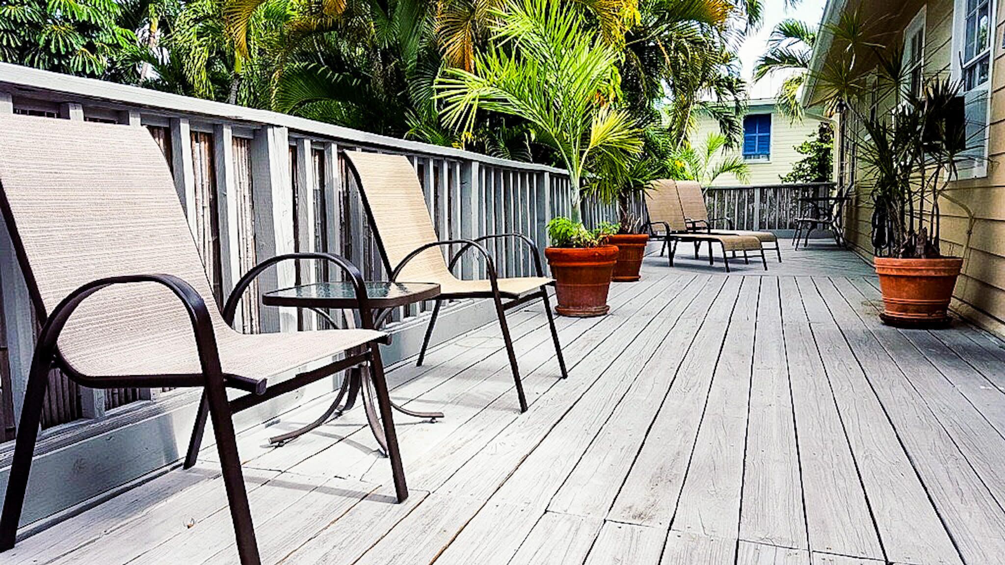 An outdoor patio with wooden flooring, metal chairs, and potted plants.