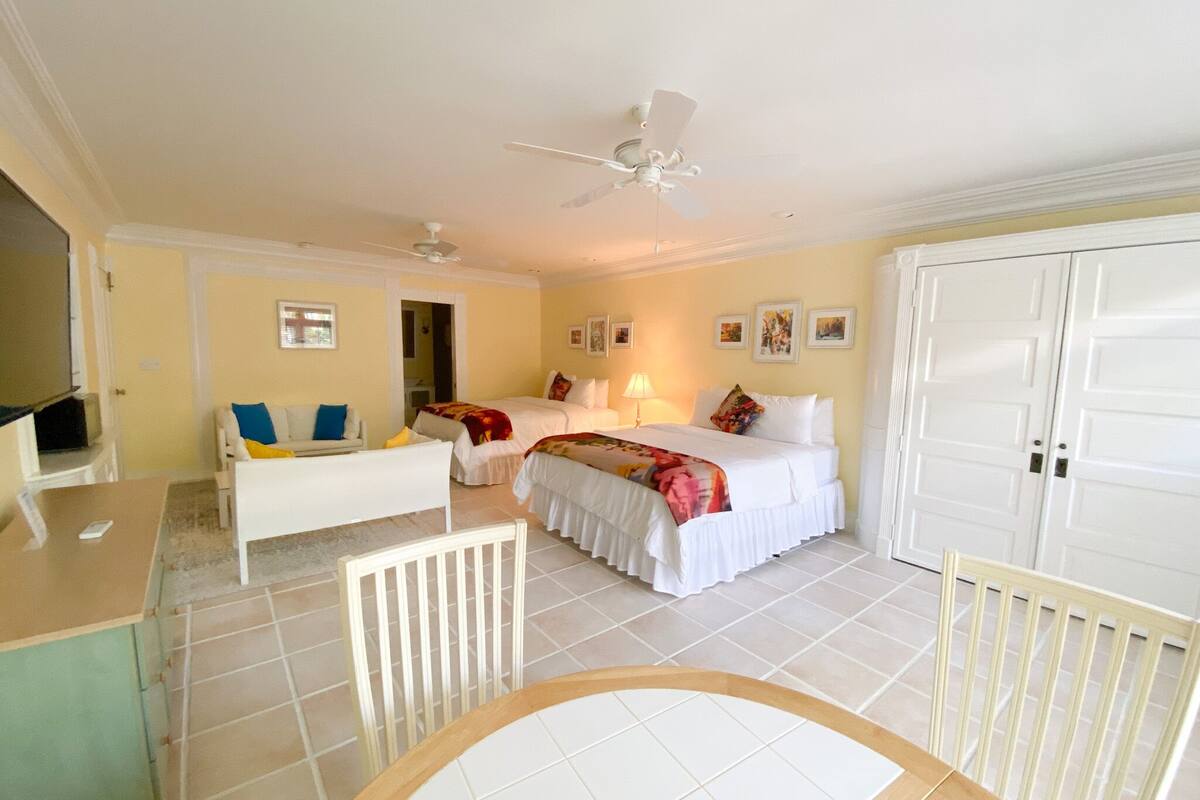 A hotel room with two beds, a desk, a chair, a TV, and a ceiling fan.