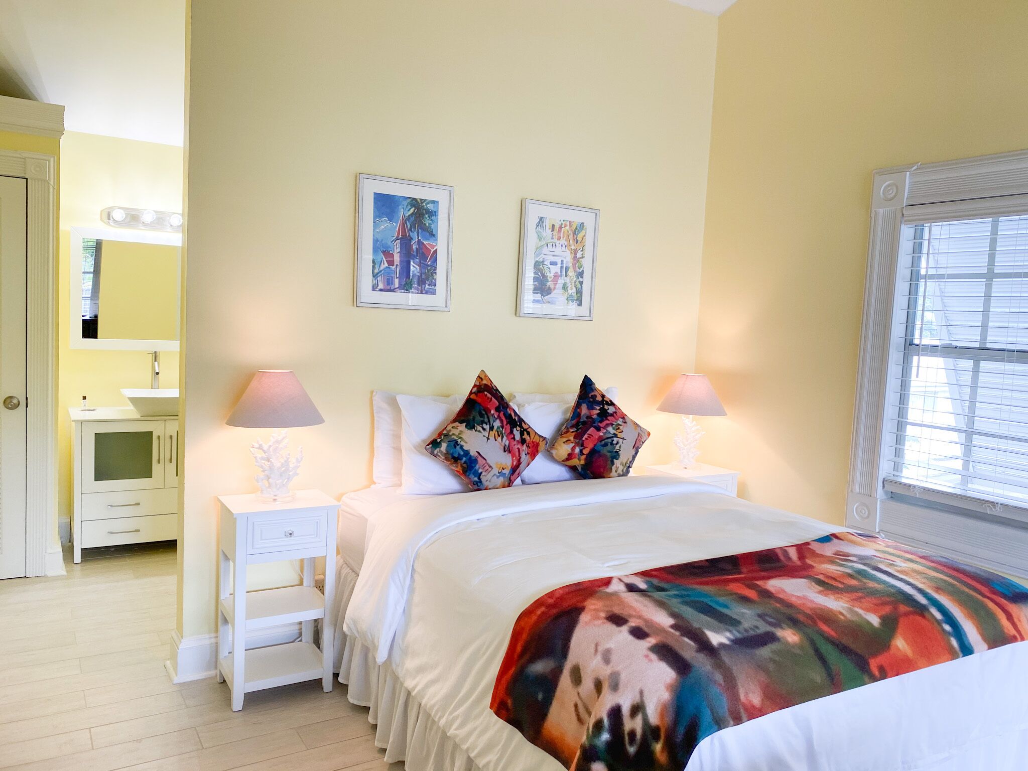Une chambre à coucher comprenant un lit, deux tables de chevet, une commode, un miroir et une fenêtre avec des stores.