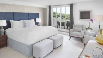 A modern hotel room with a large bed, a seating area with a chair and table, and a balcony with outdoor furniture.