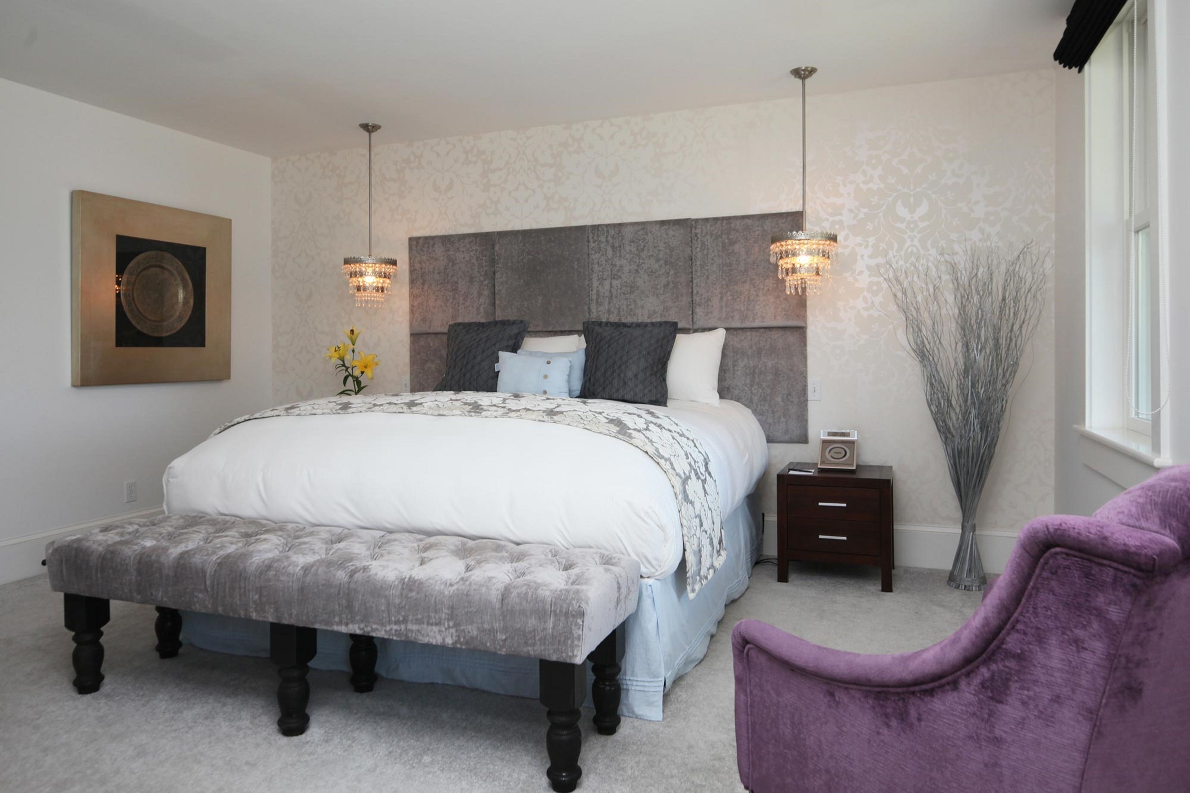 A bedroom with a large bed, bedside tables, a bench, a chair, and a window.