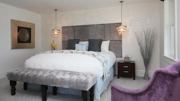A bedroom with a large bed, bedside tables, a bench, a chair, and a window.