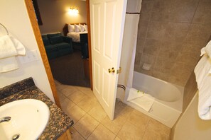 A bathroom with a sink, bathtub, and a door leading to a living area.