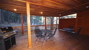 A covered outdoor area with a wooden deck, a grill, and metal tables and chairs.