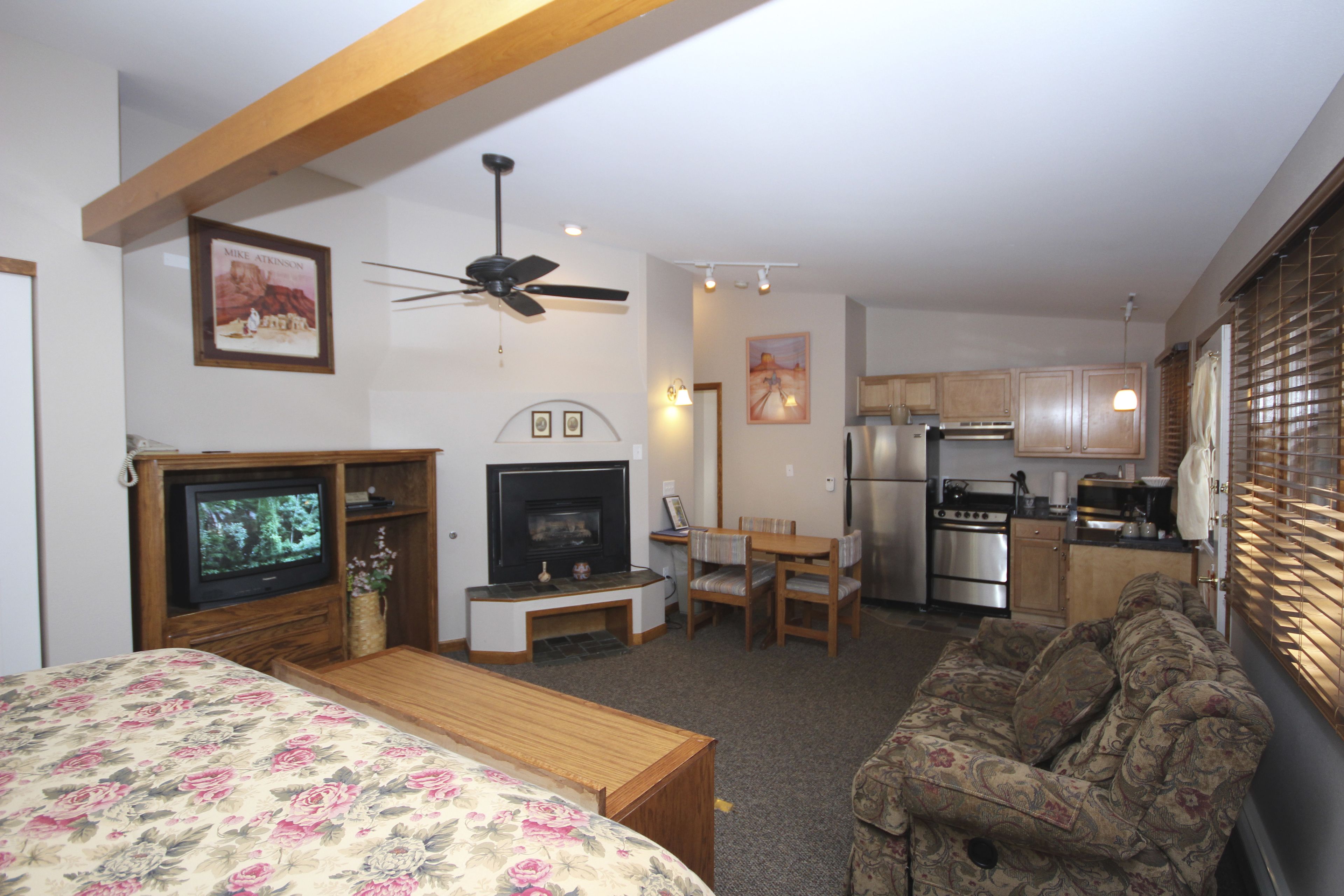 A compact living space with a bed, a TV, a fireplace, a dining area, and a kitchenette.