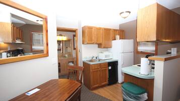 A compact kitchen with wooden cabinets, a microwave, a refrigerator, and a trash bin.