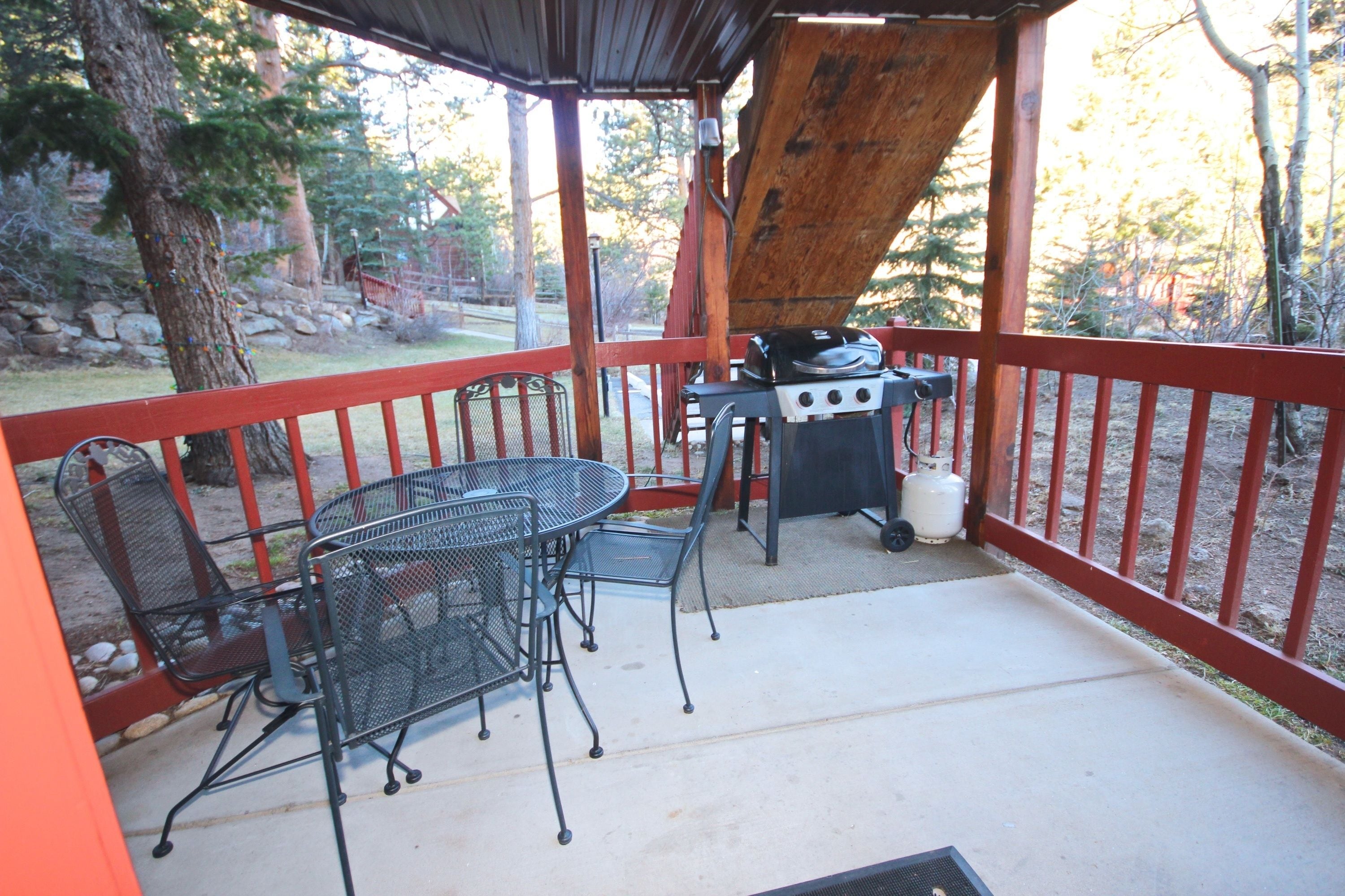 Eine überdachte Terrasse mit Grill, Metallstühlen und einem Tisch.