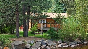 A cabin with a deck, surrounded by trees and a stream.
