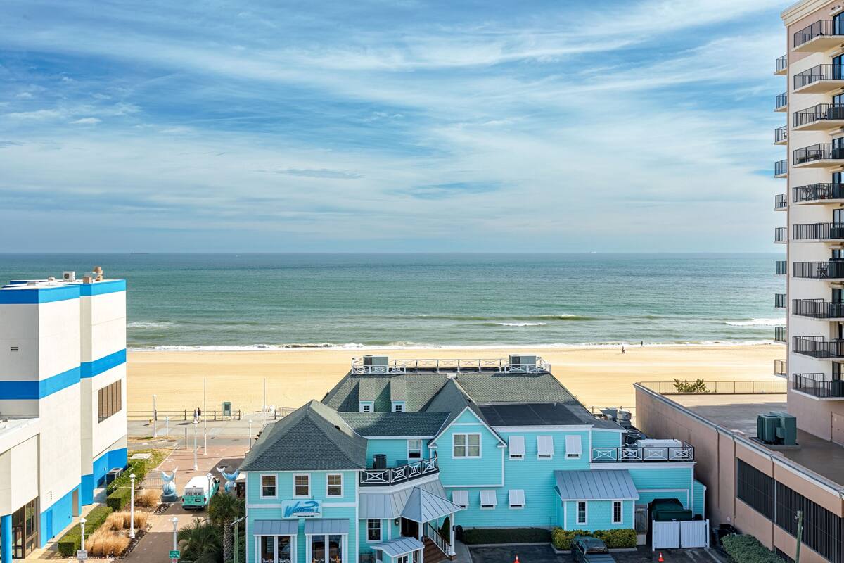 A coastal hotel with a beach view, featuring a two-story structure with balconies and a flat roof.