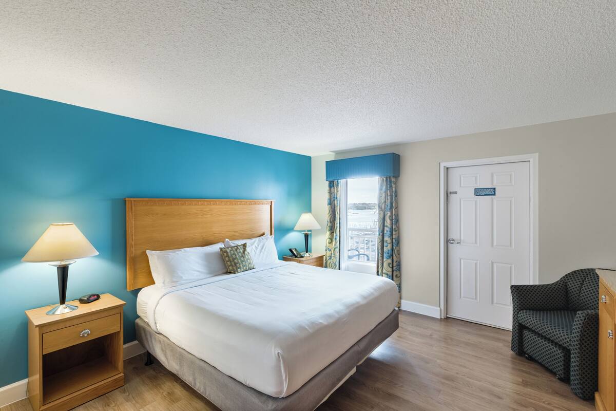 A hotel room with a large bed, bedside tables with lamps, a chair, and a door.