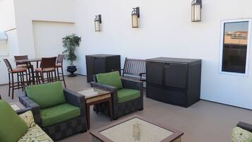 A patio area with wicker furniture, including chairs and a table, and a large planter with a plant.