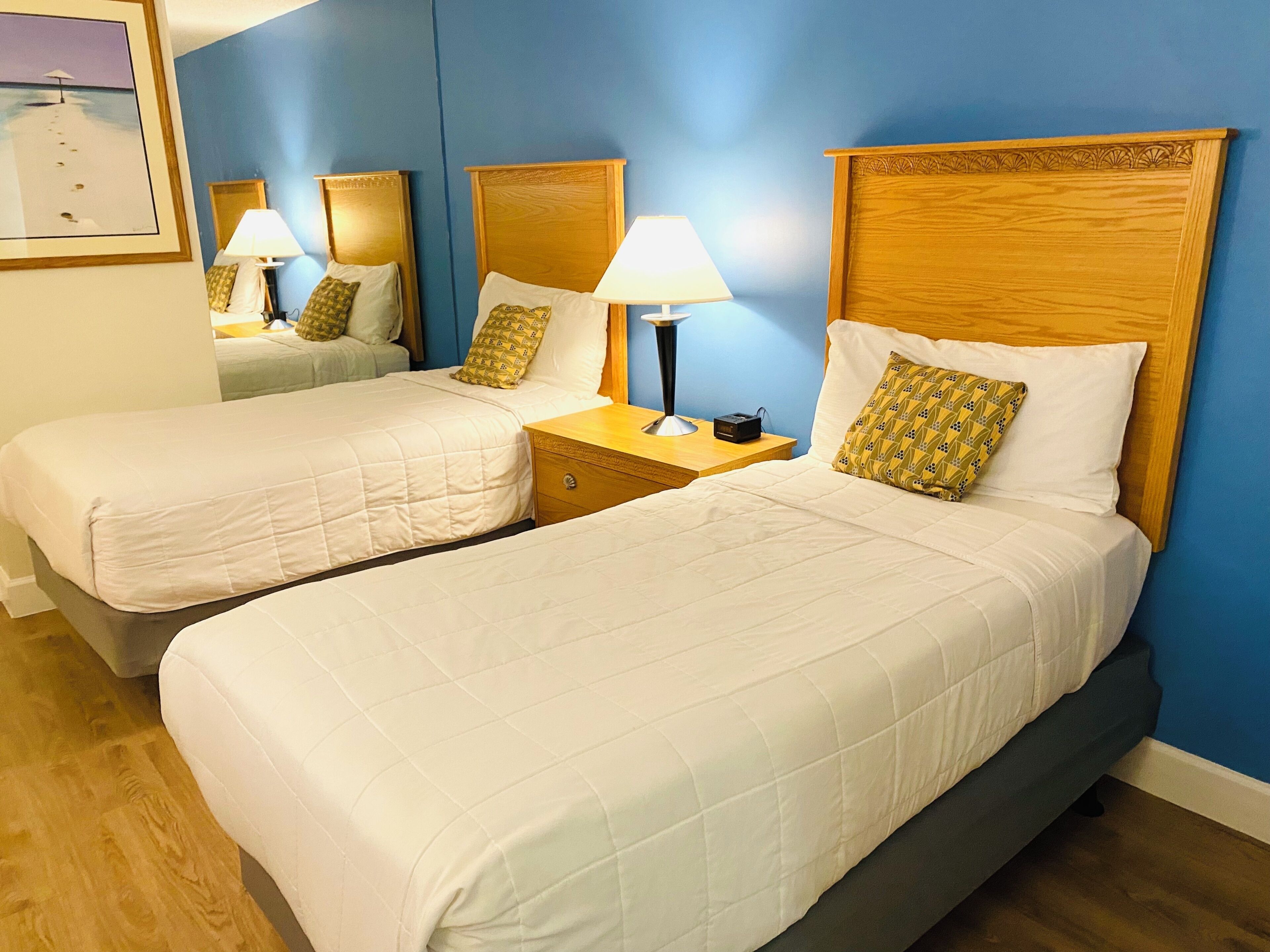 A hotel room with two beds, wooden headboards, bedside lamps, and a framed picture on the wall.