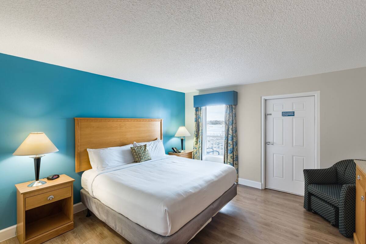 A hotel room with a large bed, bedside lamps, a wooden nightstand, a chair, and a door with a sign.