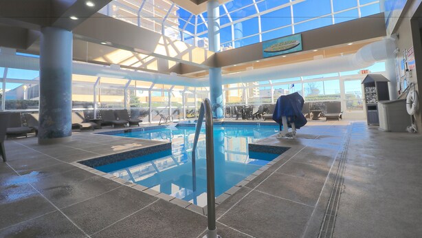 Una piscina interior con techos de vidrio transparente, sillas de descanso y vistas al exterior.