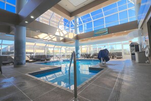An indoor swimming pool with clear glass ceilings, lounge chairs, and a view of the outside. - The Ocean Key Virginia Beach Resort (Virginia Beach)