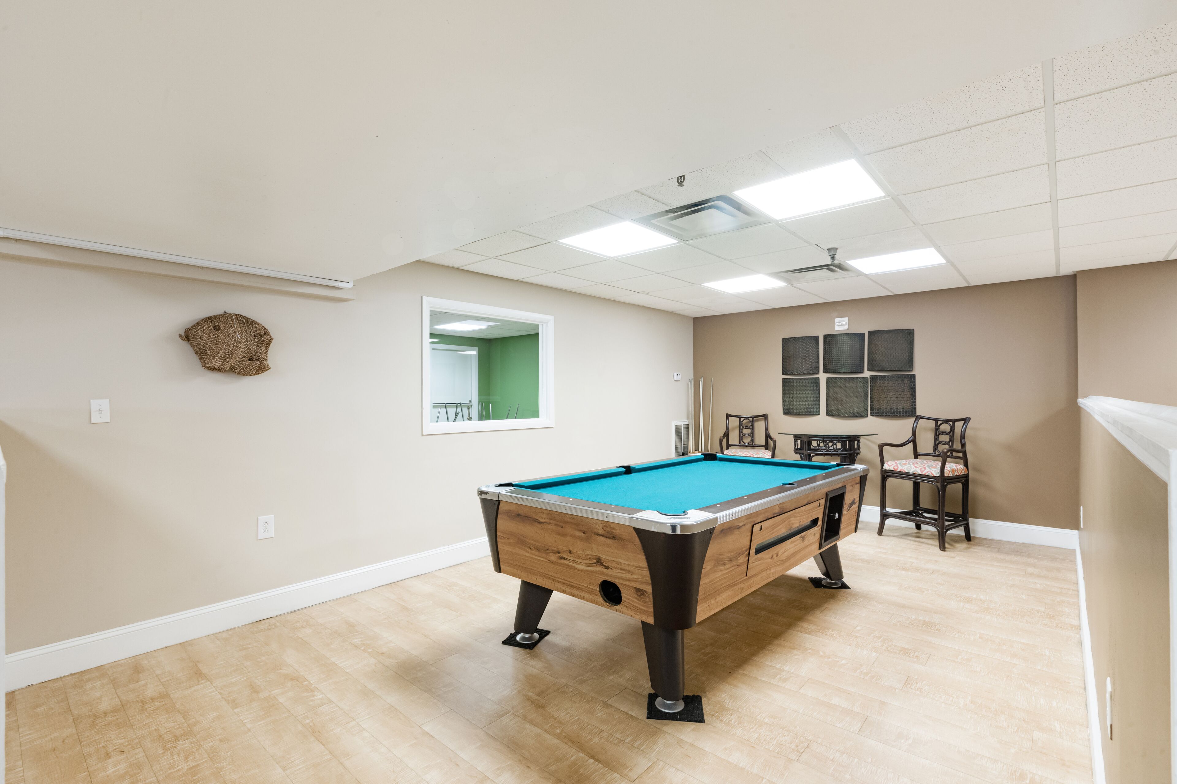A pool table in a room with a wooden floor, a ceiling fan, and a window with a green view.