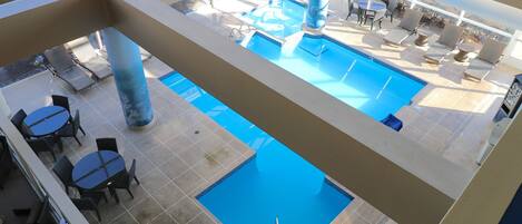 A pool area with lounge chairs and tables, a view of the pool, and a painting on the wall.