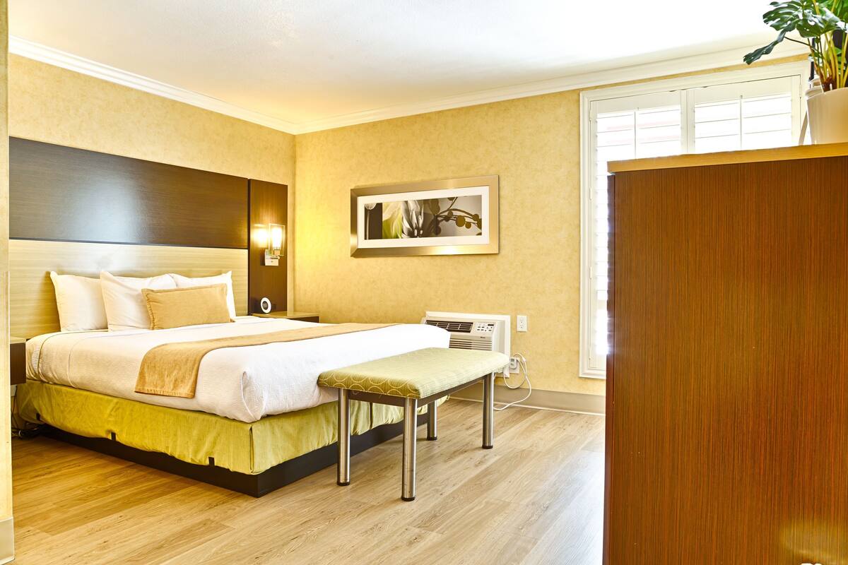 Une chambre d’hôtel équipée d’un lit, d’une table de chevet, d’un banc, d’œuvres d’art accrochées au mur et d’un appareil de climatisation.