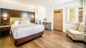 A hotel room with a large bed, bedside tables, a desk, a chair, and a door.