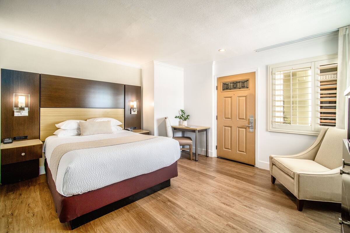 Une chambre d’hôtel avec un grand lit, des tables de chevet, un bureau, une chaise et une porte.