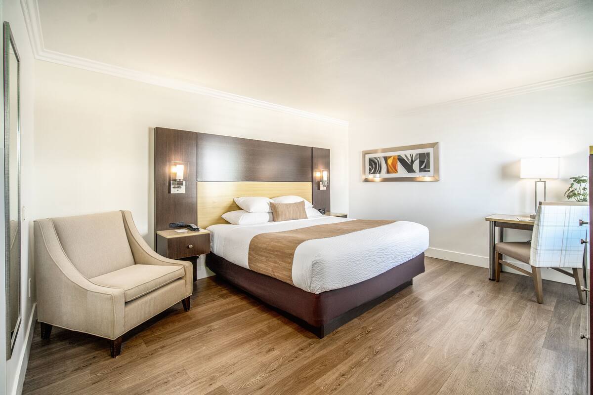 Une chambre d’hôtel avec un grand lit, une table de chevet, une chaise et un bureau avec une lampe.