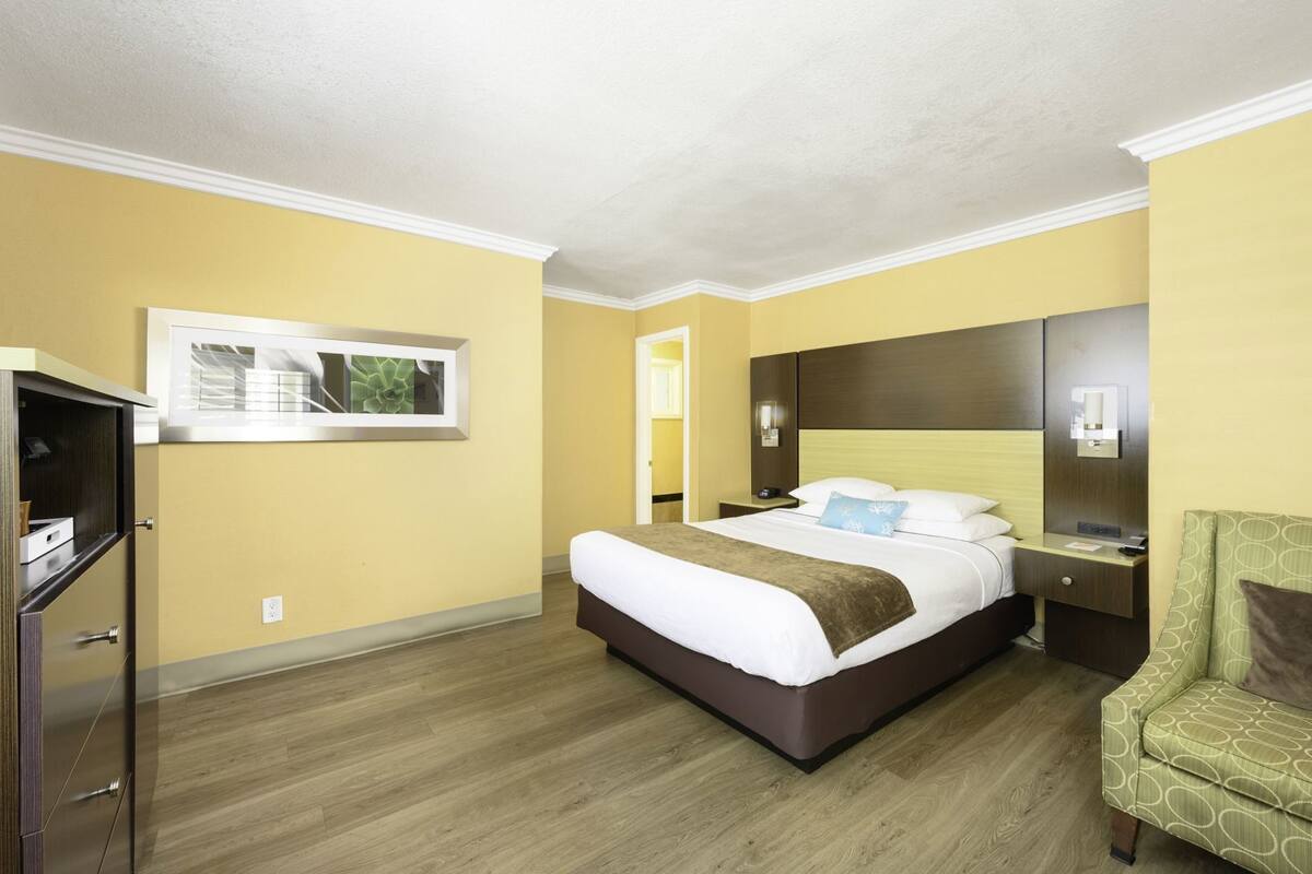 Une chambre d’hôtel équipée d’un lit, d’une table de chevet, d’une chaise et d’un téléviseur fixé au mur.