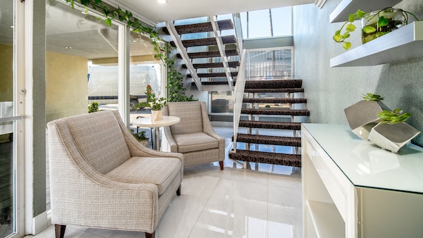 A modern interior with a staircase, wicker furniture, and potted plants.