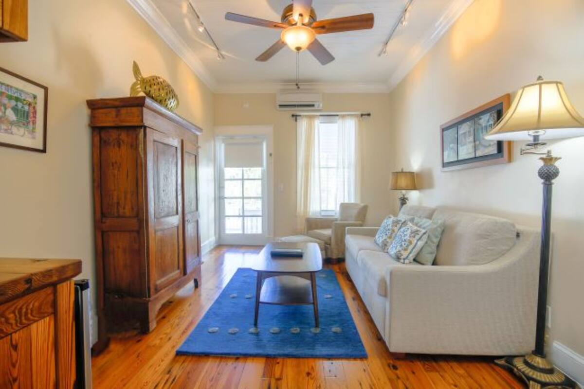 A living room with a wooden floor, a ceiling fan, a sofa, a coffee table, and a lamp.