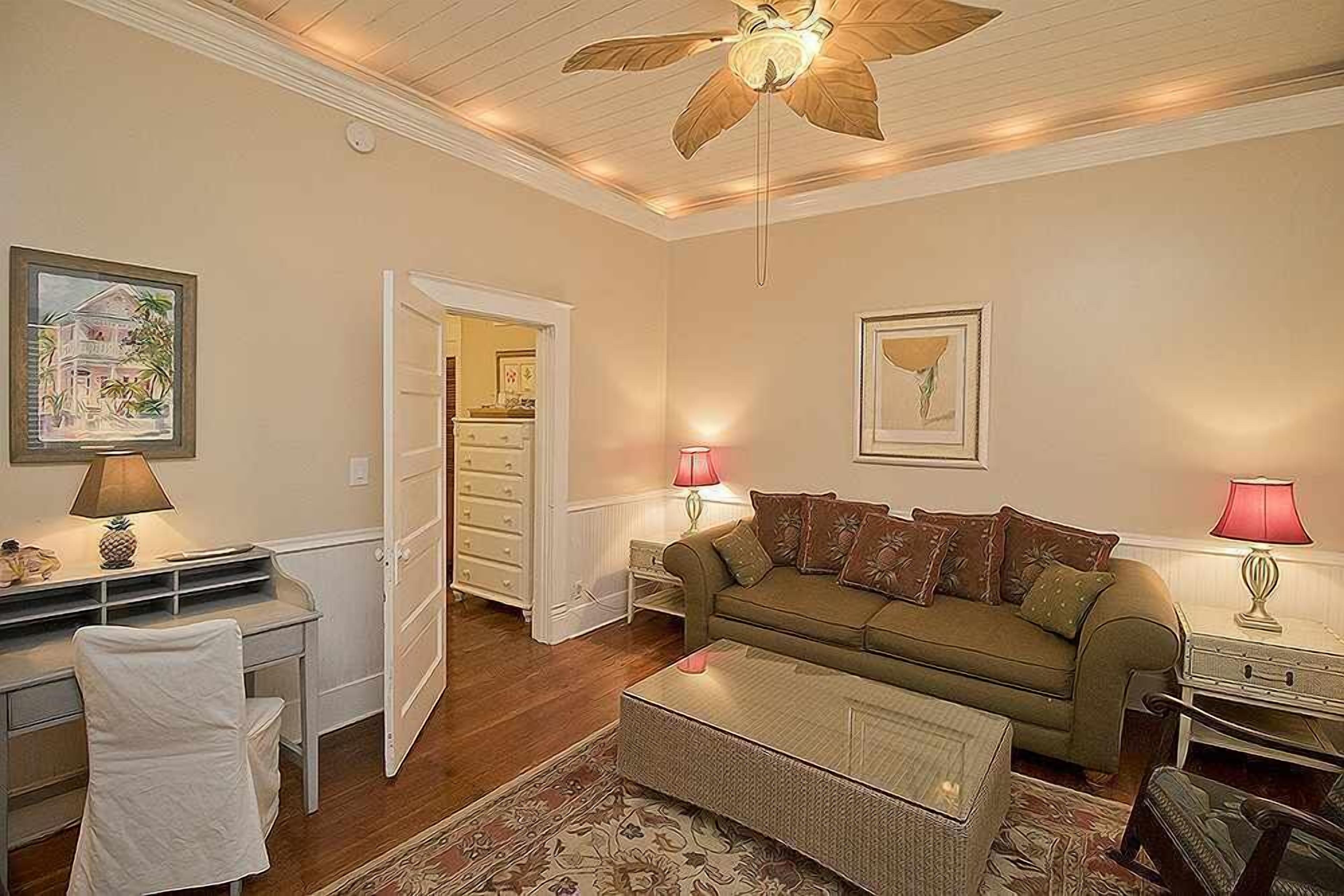 A cozy living room with a ceiling fan, a sofa, a coffee table, and a desk with a chair.