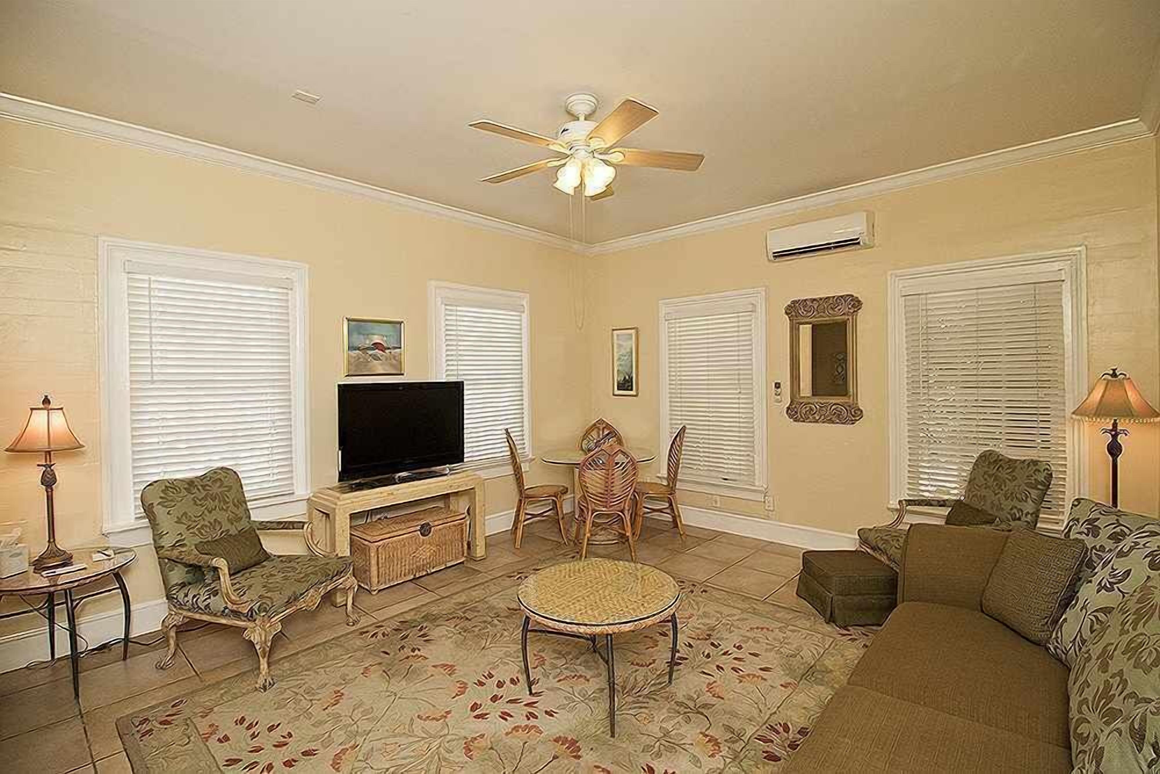 A living room with a television, two chairs, a sofa, a round table, and a ceiling fan.
