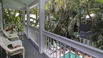 Un portico riparato con poltrone in vimini e un'amaca, con vista su una piscina e vegetazione tropicale rigogliosa.