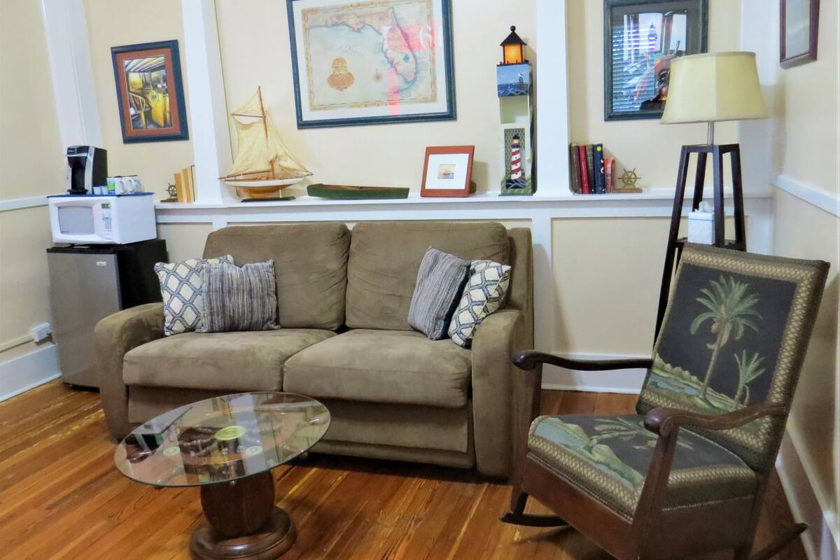 A living room with a sofa, a glass coffee table, a wooden chair, and a small side table.