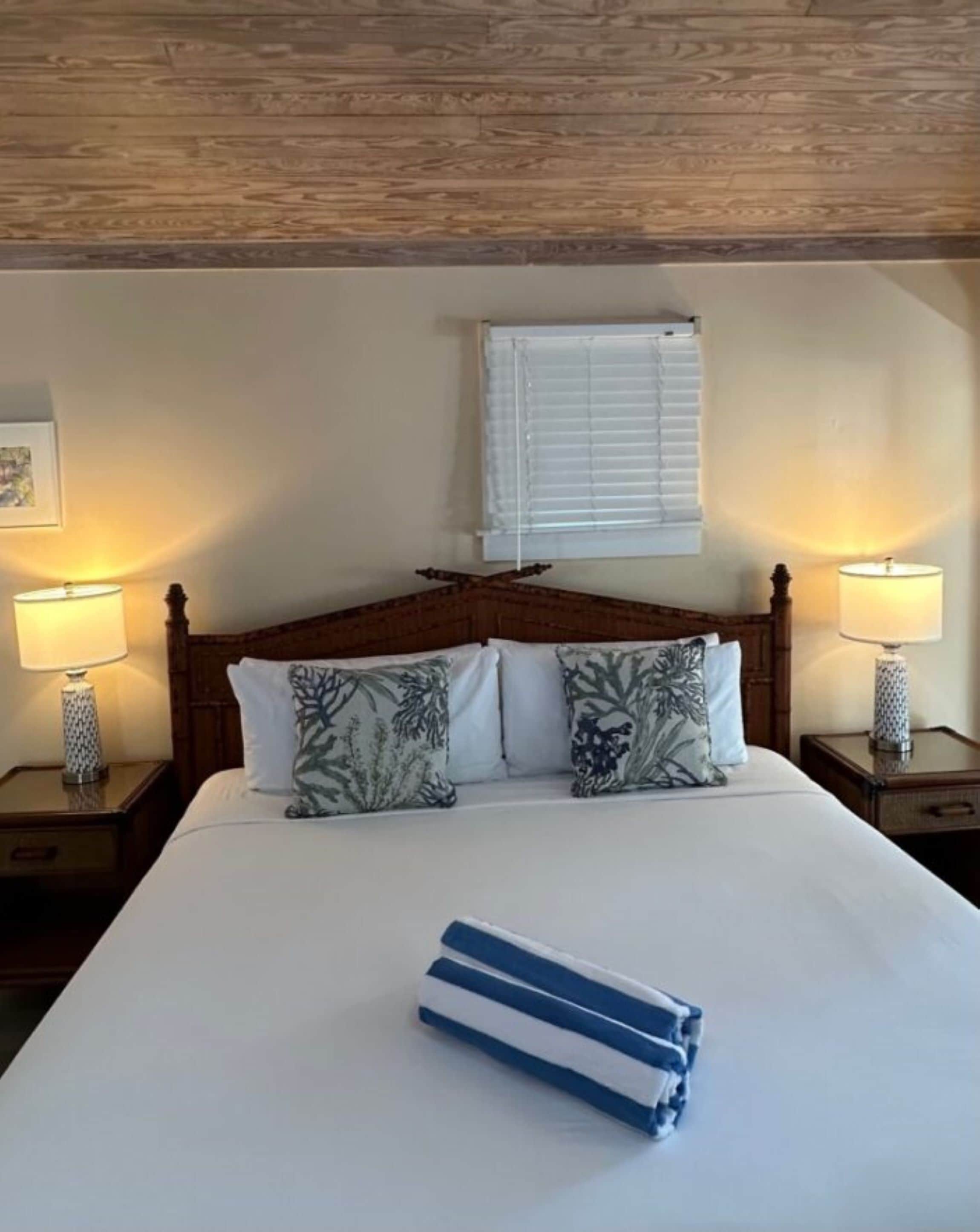 A neatly made bed with floral pillows, a wooden headboard, and two bedside lamps.
