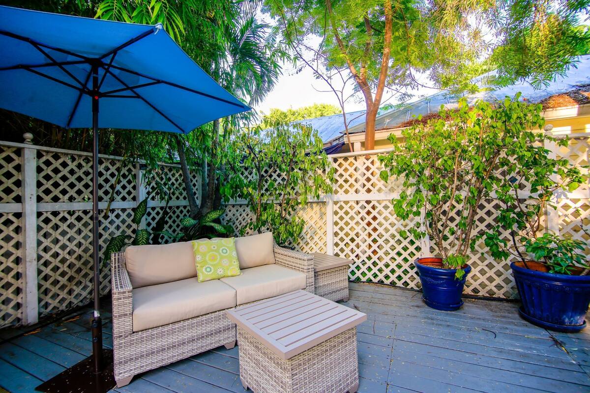A patio with a wicker sofa, a small table, and two potted plants.