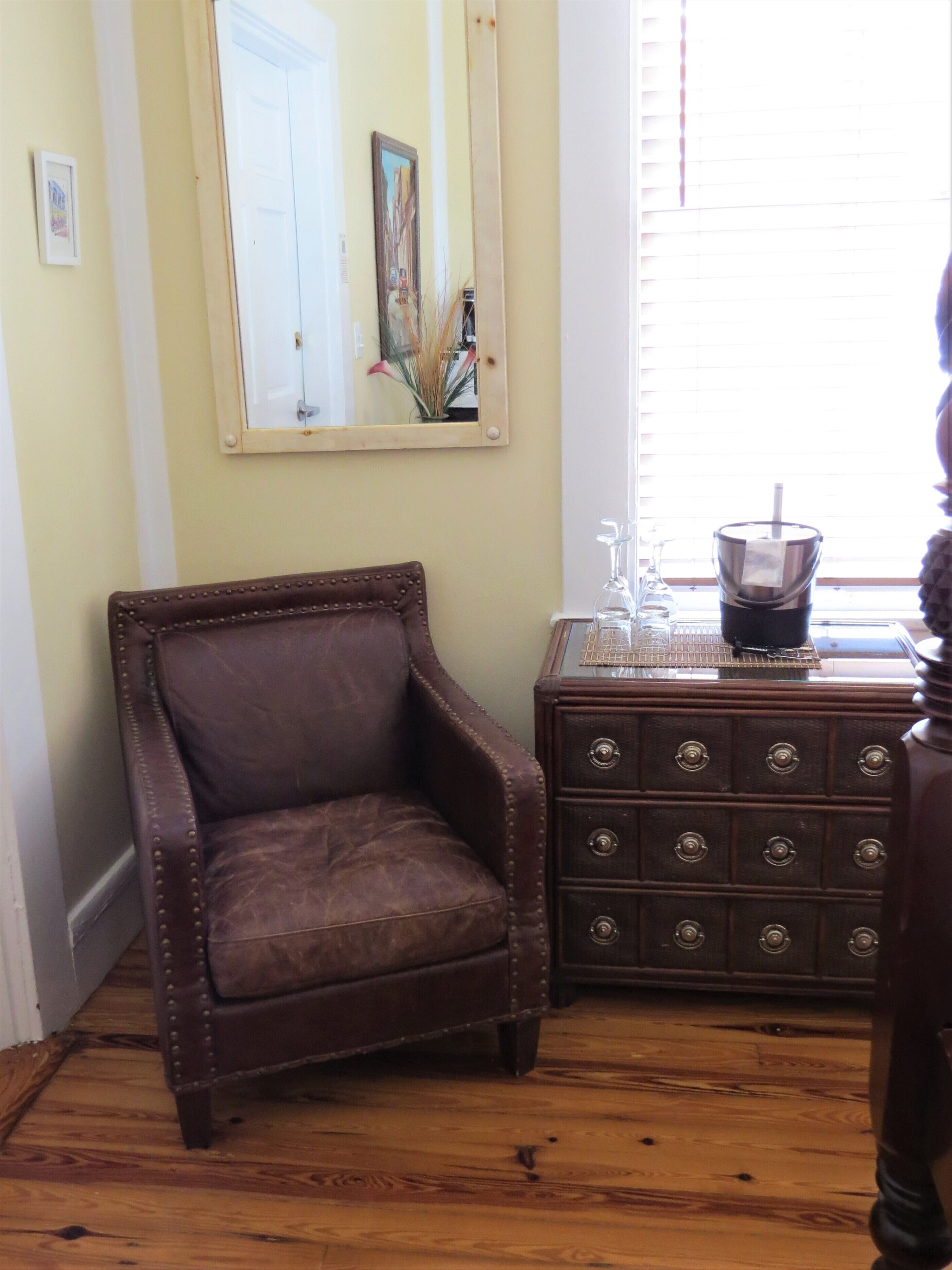 A room with a brown leather armchair, a wooden dresser with multiple drawers, and a mirror on the wall.