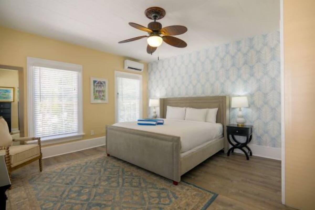 A bedroom with a bed, a ceiling fan, a nightstand, a chair, and a patterned rug.