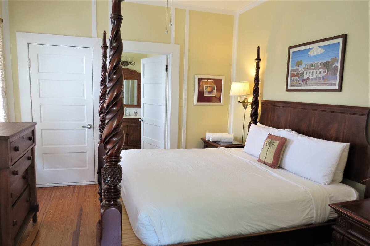 A hotel room with a four-poster bed, wooden furniture, and a painting on the wall.