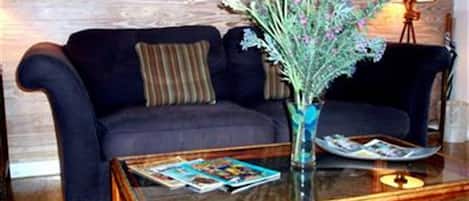 A dark blue sofa with a striped pillow, a glass coffee table with magazines, and a vase with flowers.