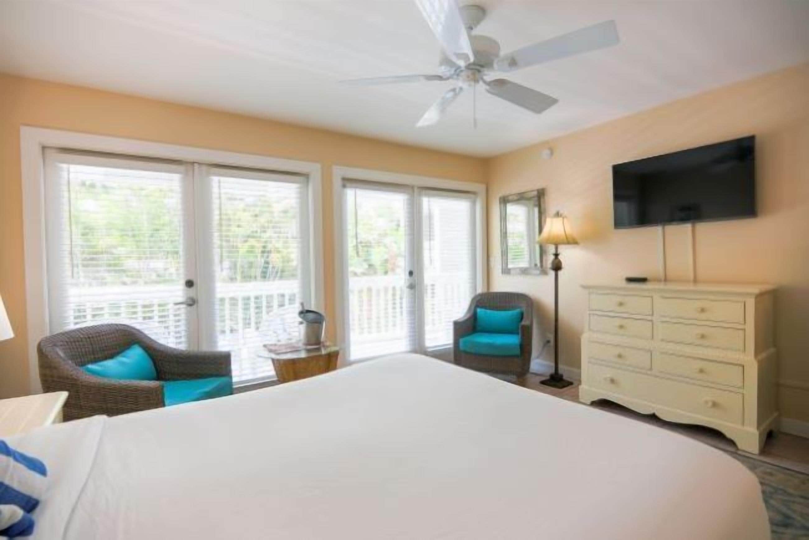 A hotel room with a large bed, a ceiling fan, a TV, a dresser, and a chair.