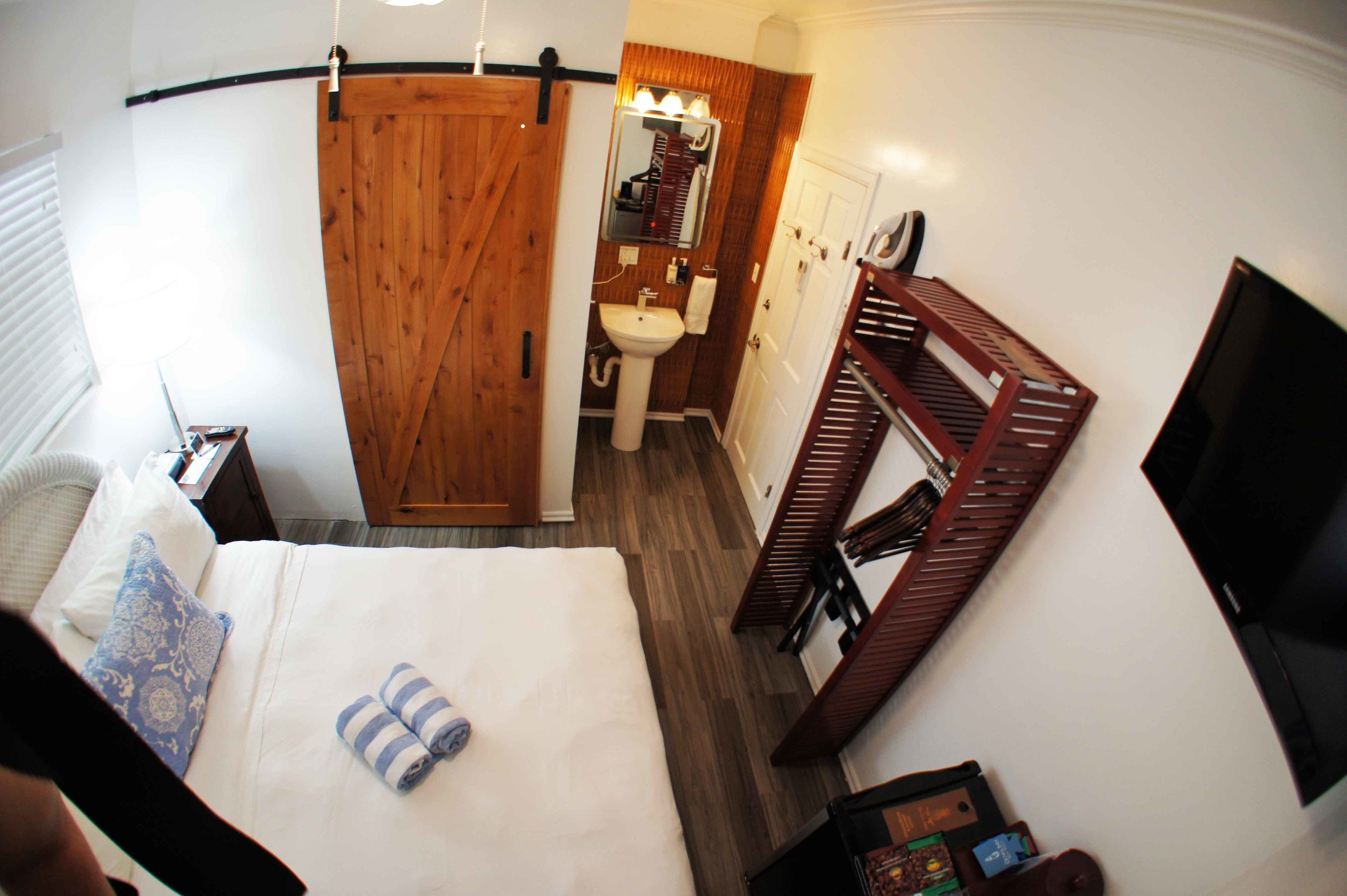 Habitación de hotel con una cama, un armario de madera, baño con lavabo y espejo, y un televisor en la pared.