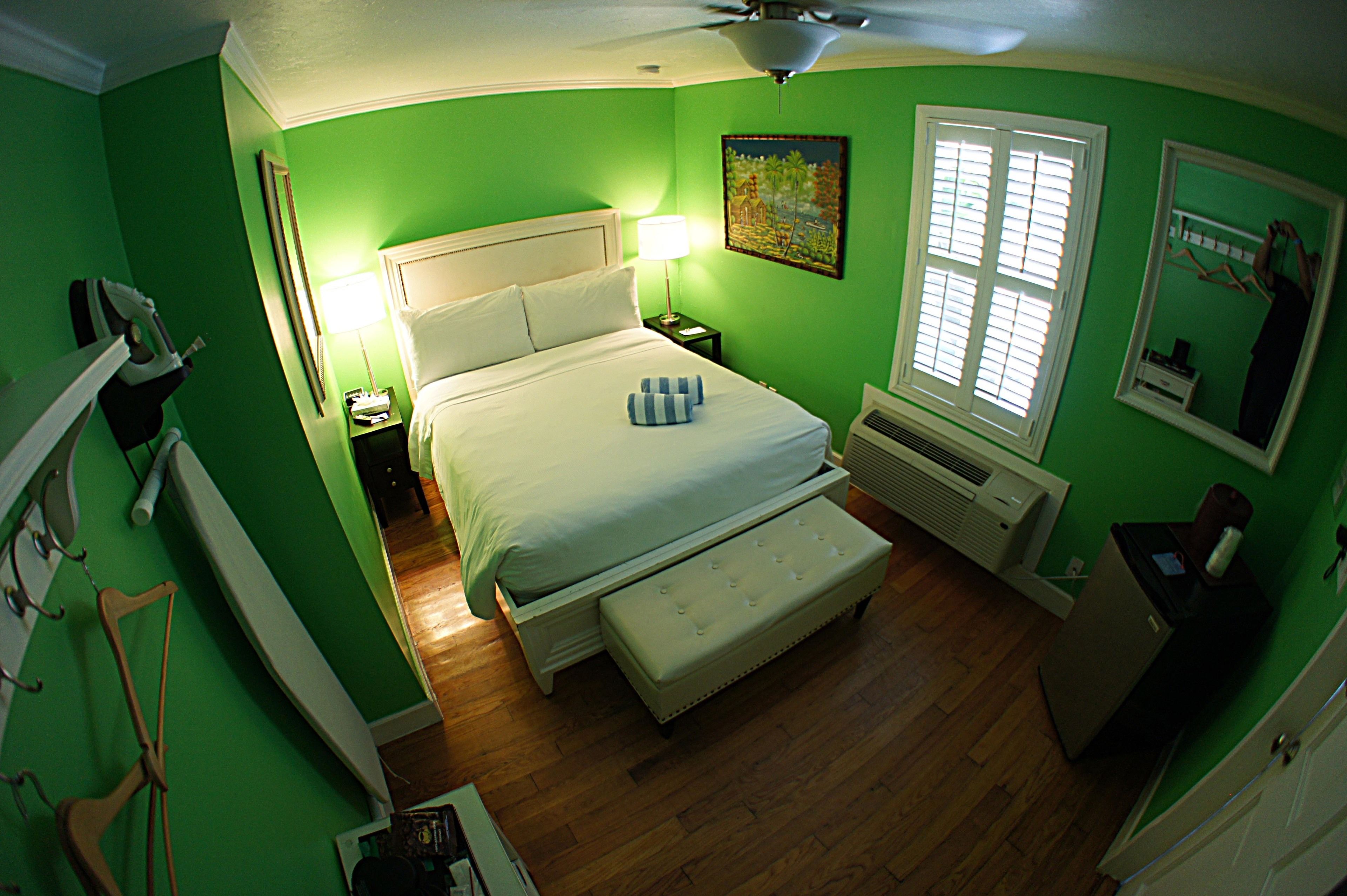 A room with a bed, a nightstand, a lamp, a window with blinds, a heater, and a small cabinet.