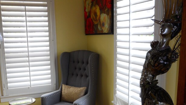 Una habitación con suelo de madera, un sillón tapizado gris con un cojín estampado, una pequeña mesa redonda y una escultura decorativa.
