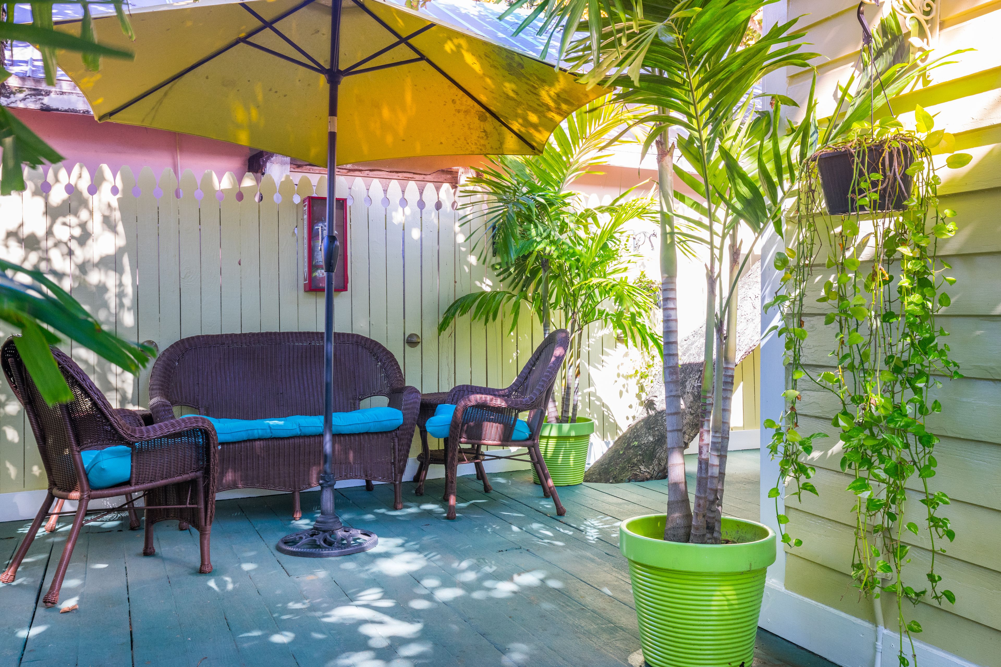 A patio with wicker furniture, a hanging plant, and a yellow umbrella.