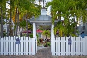 A gated entrance with a gazebo, palm trees, and a brick pathway leading to a building with a red roof. - Duval Inn (Key West)